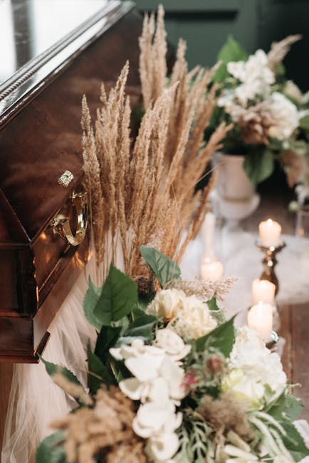 A floral arrangement for sympathy, featuring large white roses, pale pink roses, and white hydrangeas in elegant white vases on either side of a polished wooden casket. The flowers are complemented by